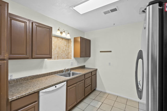 kitchen featuring sink, a skylight, light tile patterned floors, stainless steel refrigerator, and dishwasher