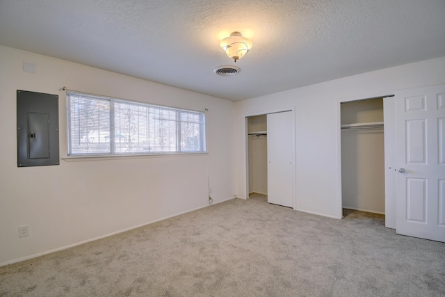 unfurnished bedroom with light colored carpet, electric panel, multiple closets, and a textured ceiling