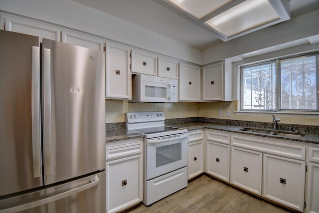 kitchen with white cabinetry, sink, backsplash, dark stone counters, and white appliances