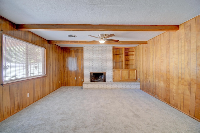 unfurnished living room with wooden walls, a fireplace, beam ceiling, and a textured ceiling