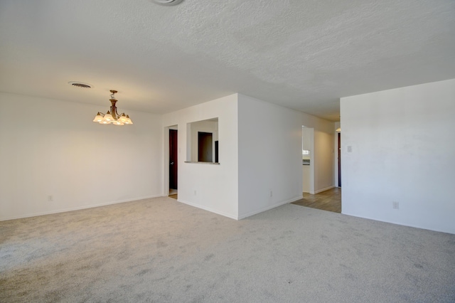 carpeted empty room with a textured ceiling and a chandelier