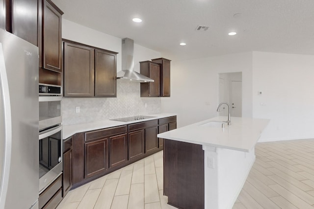 kitchen with sink, fridge, wall chimney range hood, a kitchen island with sink, and backsplash