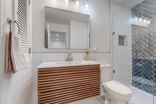 bathroom with tiled shower, vanity, toilet, and tile walls