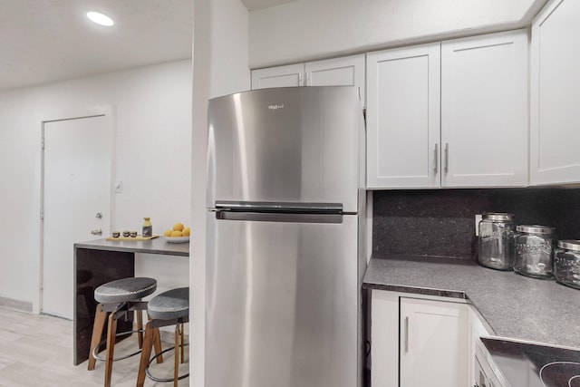 kitchen with stainless steel refrigerator, white cabinetry, light wood-type flooring, and stove