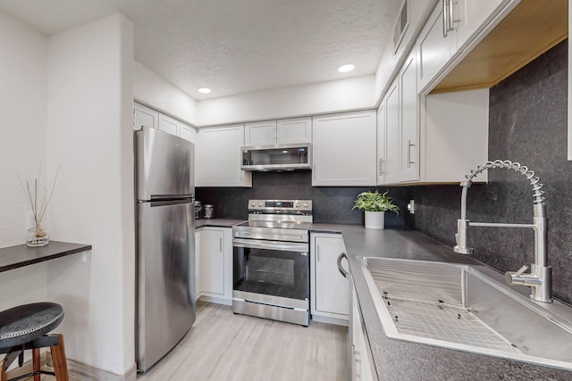 kitchen with appliances with stainless steel finishes, white cabinetry, sink, decorative backsplash, and a textured ceiling