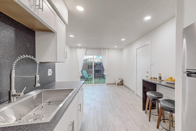 kitchen featuring light hardwood / wood-style floors, refrigerator, sink, and white cabinets