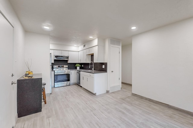 kitchen featuring sink, white cabinetry, tasteful backsplash, light wood-type flooring, and appliances with stainless steel finishes