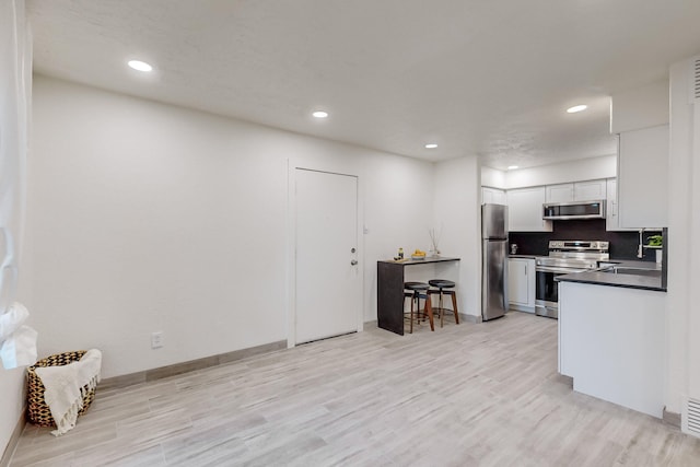 kitchen featuring stainless steel appliances, decorative backsplash, white cabinets, and light hardwood / wood-style flooring