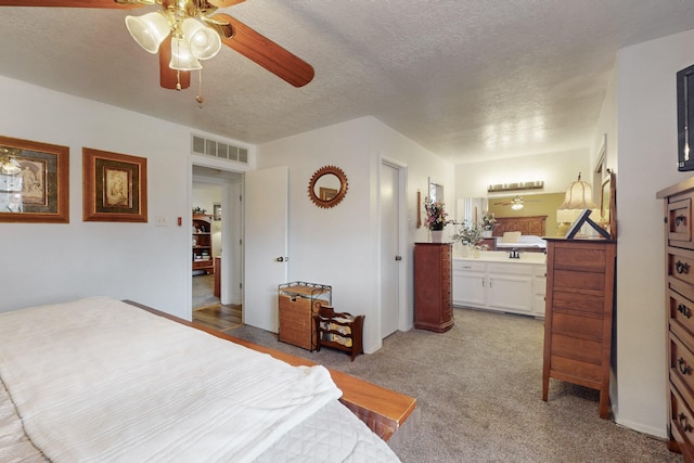 bedroom featuring visible vents, ensuite bath, light carpet, and a textured ceiling