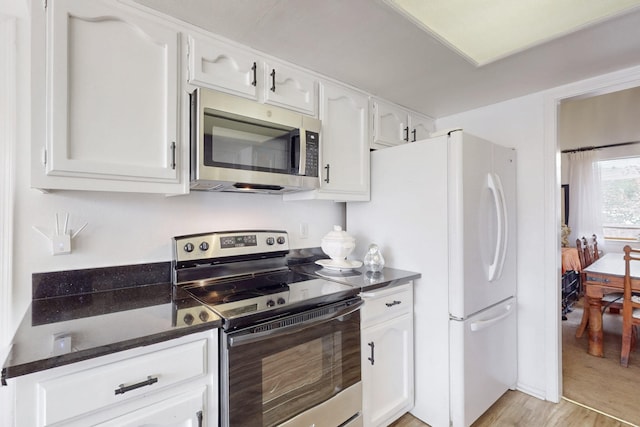 kitchen with appliances with stainless steel finishes, light wood-type flooring, white cabinetry, and dark stone counters