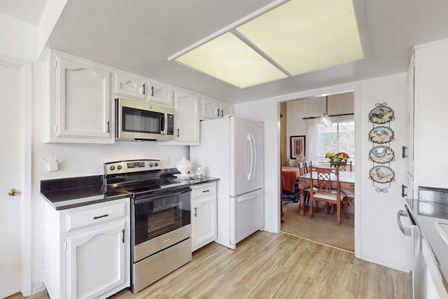 kitchen featuring stainless steel appliances, light wood finished floors, dark countertops, and white cabinets