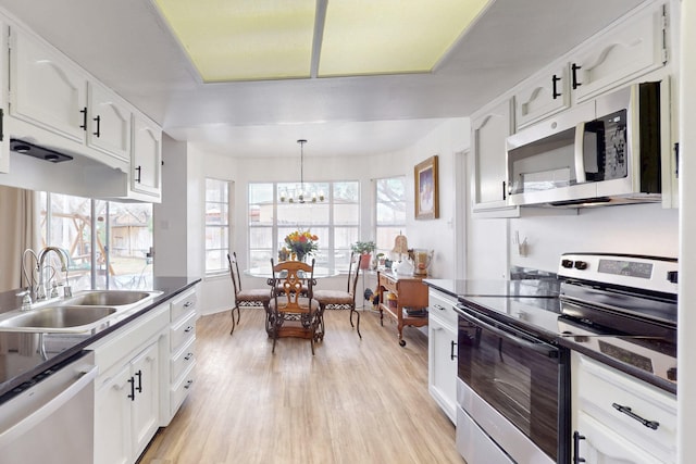 kitchen featuring dark countertops, appliances with stainless steel finishes, light wood-style floors, white cabinetry, and a sink