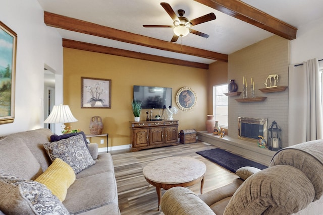 living area with baseboards, ceiling fan, wood finished floors, a fireplace, and beam ceiling