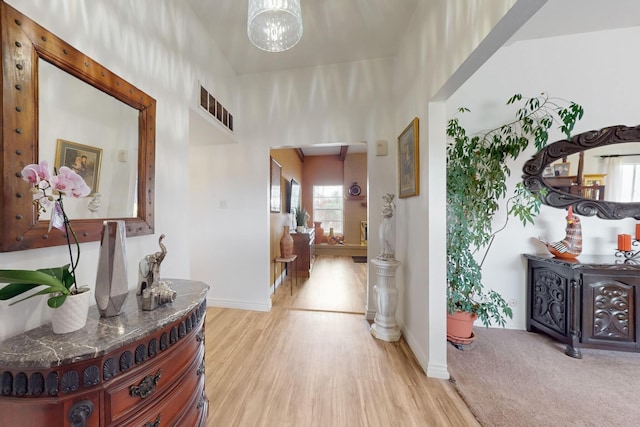 hallway with a notable chandelier, light wood-type flooring, visible vents, and baseboards