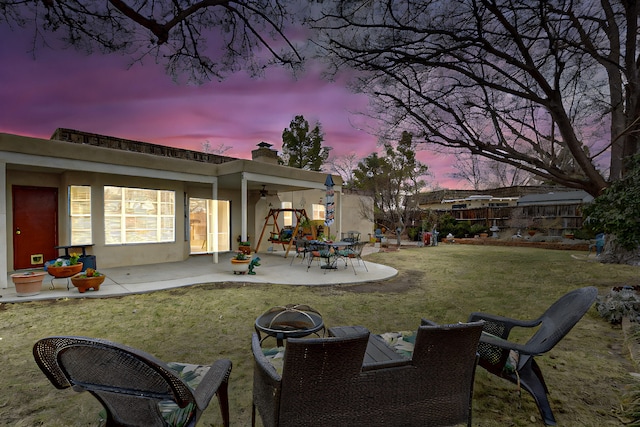 yard at dusk featuring a patio area, ceiling fan, a fire pit, and fence