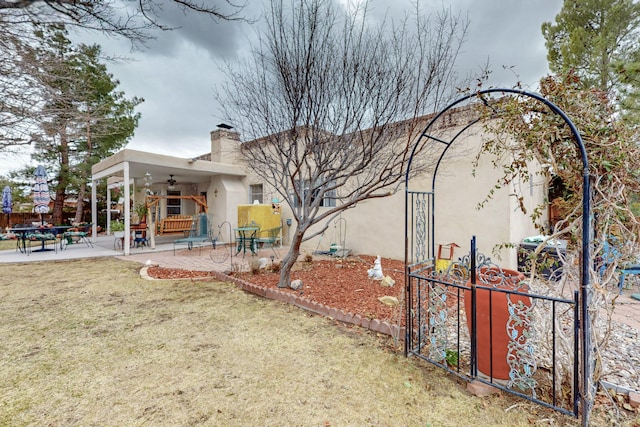 rear view of property featuring ceiling fan, a yard, stucco siding, a chimney, and a patio area