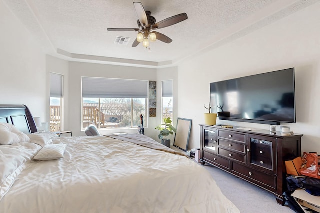 carpeted bedroom featuring a raised ceiling, ceiling fan, and a textured ceiling