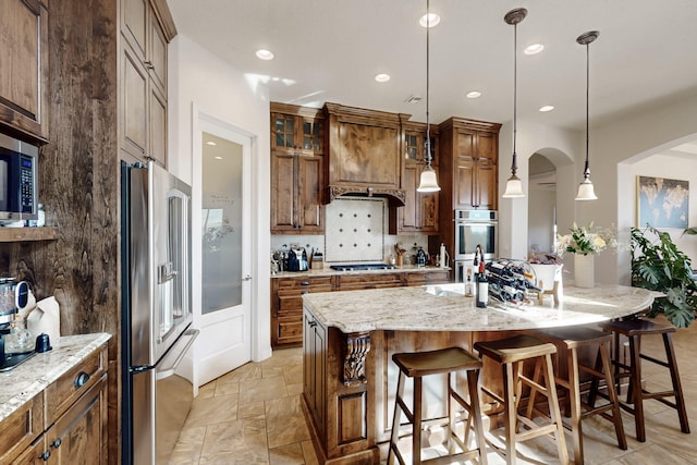 kitchen with a breakfast bar, pendant lighting, backsplash, stainless steel appliances, and a center island with sink