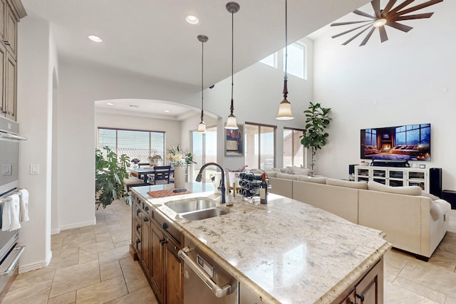 kitchen featuring an island with sink, dishwasher, sink, hanging light fixtures, and light stone countertops