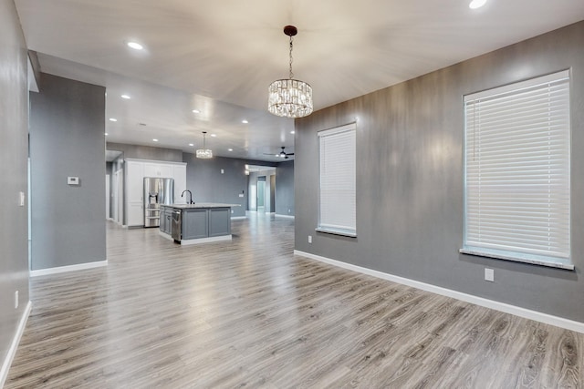 unfurnished living room with a notable chandelier, sink, and light hardwood / wood-style floors