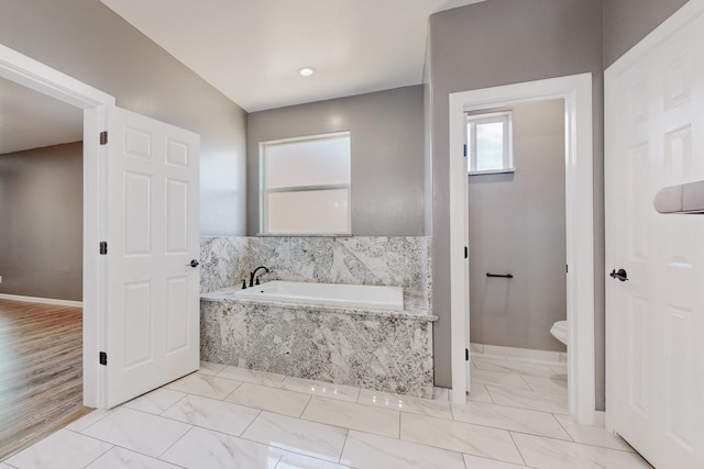 bathroom with a relaxing tiled tub and toilet