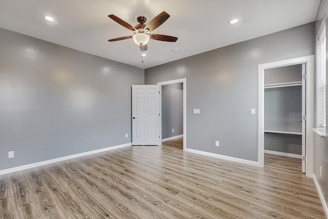 unfurnished bedroom featuring light wood-type flooring, a spacious closet, ceiling fan, and a closet