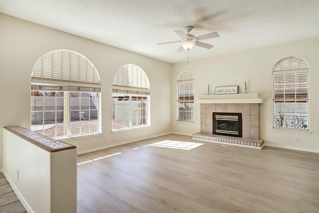 unfurnished living room with ceiling fan, a healthy amount of sunlight, a fireplace, and light hardwood / wood-style flooring