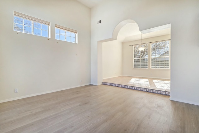 empty room featuring a towering ceiling, a chandelier, and light wood-type flooring