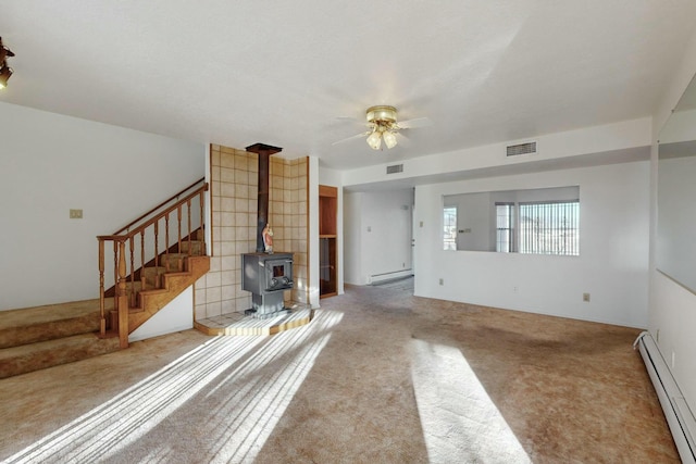 unfurnished living room featuring baseboard heating, ceiling fan, light carpet, and a wood stove