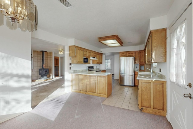 kitchen with range, light carpet, a wood stove, stainless steel fridge, and kitchen peninsula