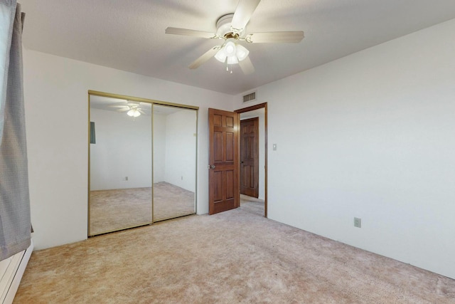 unfurnished bedroom featuring light carpet, a baseboard radiator, a closet, and ceiling fan