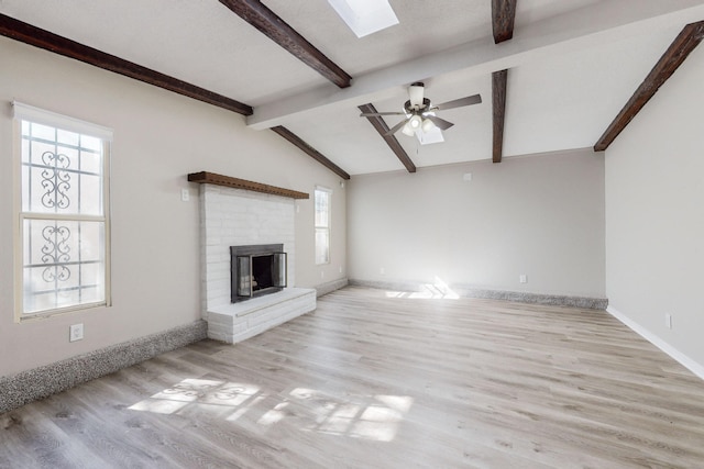 unfurnished living room featuring lofted ceiling with skylight, a brick fireplace, ceiling fan, and light wood-type flooring