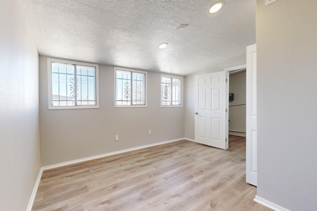 spare room featuring vaulted ceiling, a textured ceiling, and light hardwood / wood-style floors