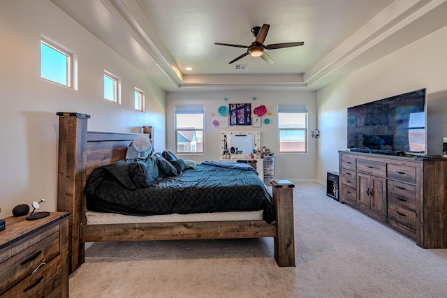 bedroom with light colored carpet, ceiling fan, and a tray ceiling