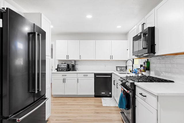 kitchen with decorative backsplash, light wood-style floors, light countertops, black appliances, and white cabinetry