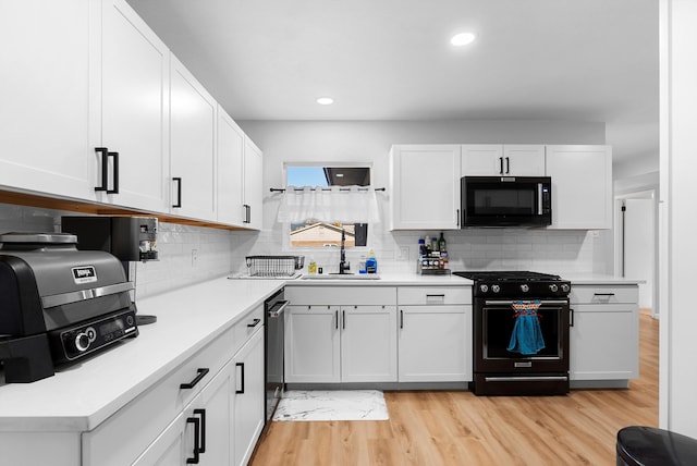 kitchen with white cabinets, light countertops, light wood-type flooring, black appliances, and a sink