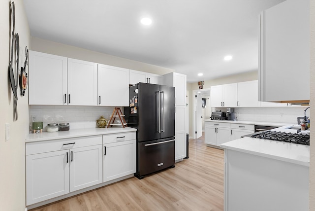 kitchen with light countertops, high end black refrigerator, light wood-style flooring, and white cabinets