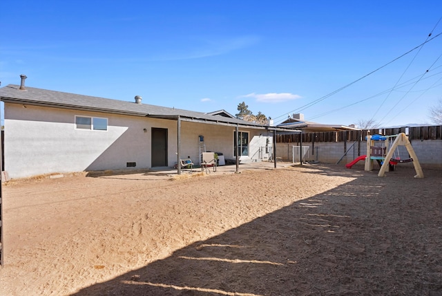 rear view of property with fence, a playground, and stucco siding