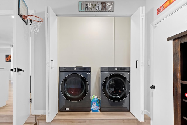 clothes washing area with washing machine and dryer and light hardwood / wood-style flooring