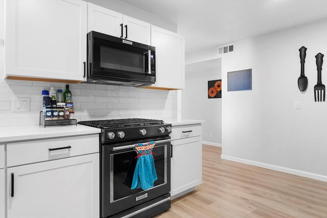 kitchen with light hardwood / wood-style flooring, white cabinets, gas range oven, and decorative backsplash