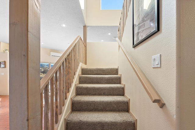 stairway with a wall mounted air conditioner and a textured ceiling