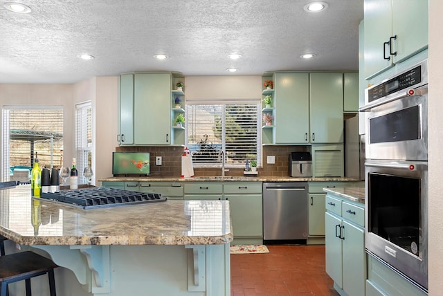 kitchen featuring a breakfast bar, sink, backsplash, green cabinetry, and stainless steel appliances