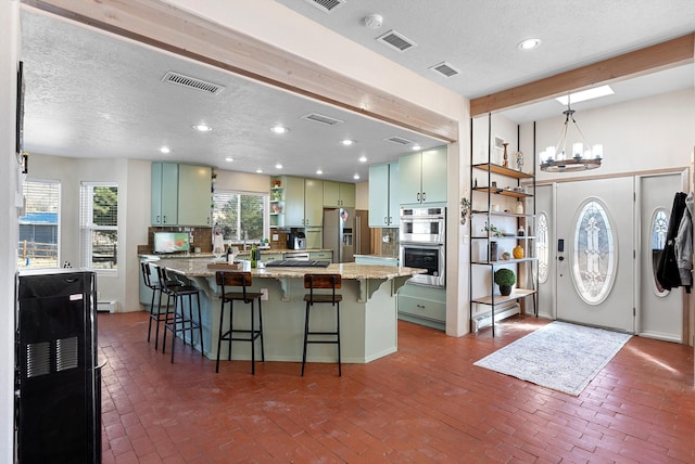 kitchen featuring stainless steel appliances, light stone countertops, green cabinets, and a kitchen island