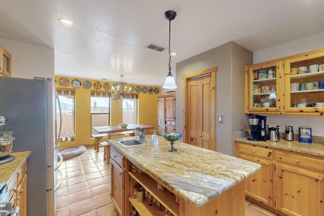 kitchen with sink, light stone countertops, an island with sink, and stainless steel refrigerator