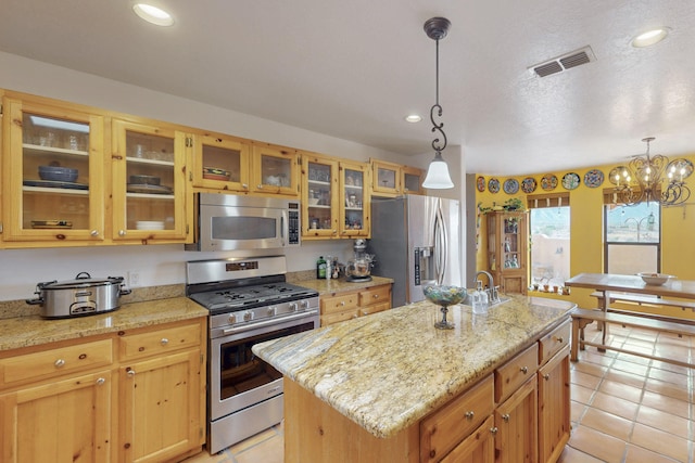 kitchen featuring light stone counters, stainless steel appliances, an island with sink, and pendant lighting