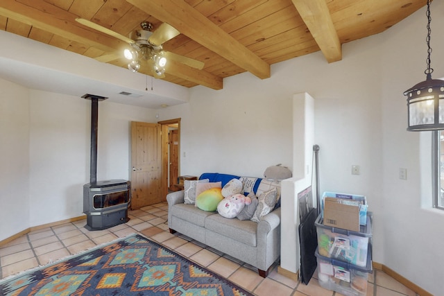 living room featuring wood ceiling, light tile patterned floors, a wood stove, ceiling fan, and beam ceiling