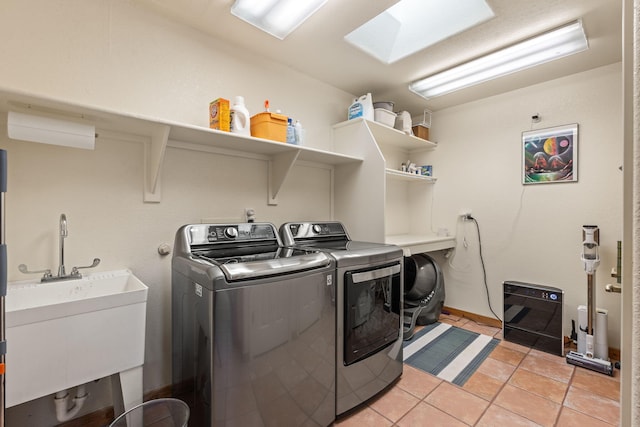 clothes washing area with sink, light tile patterned floors, a skylight, and washing machine and clothes dryer