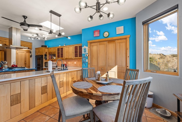 tiled dining room featuring ceiling fan with notable chandelier, a skylight, and sink