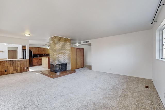 unfurnished living room featuring a brick fireplace, light colored carpet, and ceiling fan