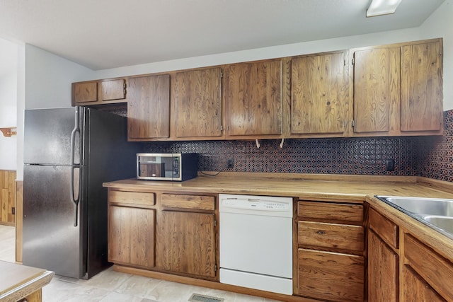 kitchen with white dishwasher, sink, decorative backsplash, and black refrigerator